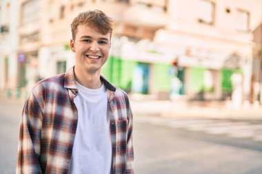Genç beyaz adam gülümseyerek şehirde mutlu mesut duruyor..