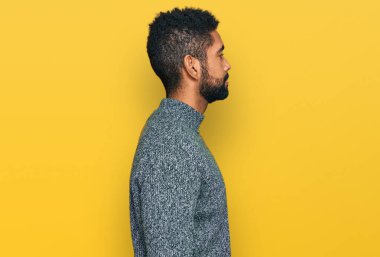 Afro-Amerikalı genç bir adam günlük giysiler giymiş, rahat bir görünüm takınıyor, doğal bir yüz ifadesi ve kendine güvenen bir gülümsemeyle poz veriyor.. 