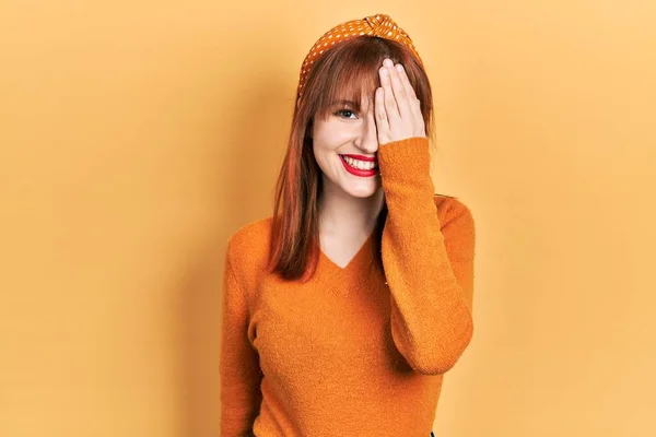 红头发的年轻女子 身穿宽松的橙色毛衣 一只眼睛蒙着一只手 脸上挂着自信的微笑 情绪也令人惊讶 — 图库照片