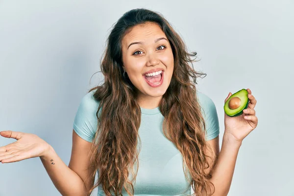 Menina Hispânica Jovem Segurando Abacate Médio Celebrando Realização Com Sorriso — Fotografia de Stock