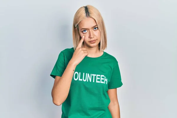 美しいブロンドの女性を着てボランティアTシャツを指差す目を見てあなたジェスチャー 怪しい表情 — ストック写真