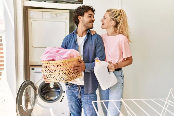 Jovem Casal Sorrindo Feliz Segurando Cesta Roupa Garrafa Detergente Casa — Fotografia de Stock