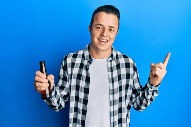 Yakışıklı genç adam yarım litre bira içiyor gülümsüyor mutlu bir şekilde elini ve parmağını yana doğru gösteriyor. 