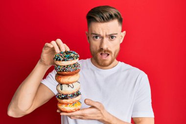 Genç kızıl saçlı adam şok olmuş suratında lezzetli renkli çörekler tutuyor. Şüpheci ve alaycı görünüyor, ağzı açık kalınca şaşırıyor. 