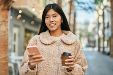 Genç Asyalı kadın akıllı telefon kullanıyor ve şehirde kahve içiyor..