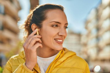 Şehirde kulaklık takarak mutlu gülümseyen genç İspanyol kız..