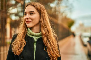 Genç sarışın kız gülümsüyor, mutlu bir şekilde şehirde duruyor..