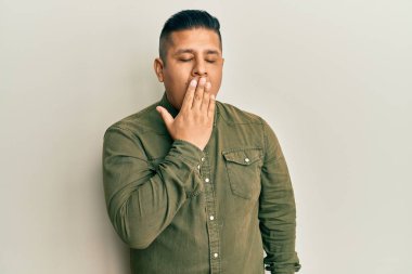 Gündelik kıyafetler giyen genç latin adam ağzıyla ağzını kapatmaktan sıkılmış. Huzursuz ve uykulu.. 