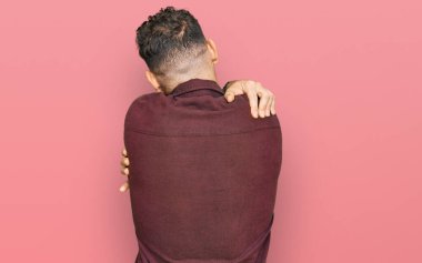 Latin kökenli genç bir adam günlük kıyafetler giyip kendine sarılıyor. Mutlu ve pozitif bir şekilde. Sevgi ve özgüven. 