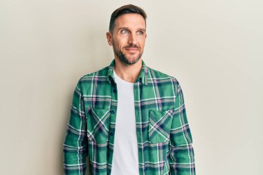 Sakallı, sıradan giyinmiş, gülümseyen, yan tarafa bakıp düşünen yakışıklı bir adam.. 