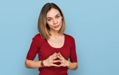 Sarışın, sıradan kıyafetler giyen genç bir kız elleri ve parmakları çapraz gülümseyerek gevşemiş ve neşeli. Başarı ve iyimserlik 