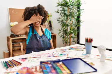 Güzel Afro saçlı Amerikalı kadın sanat stüdyosunda resim yapıyor, gülümsüyor ve yüz yüze gülüyor. Şaşırtmak için gözleri örtüyor. kör kavram. 