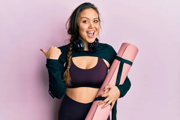 Joven Chica Hispana Usando Ropa Deportiva Sosteniendo Esterilla Yoga Apuntando —  Fotos de Stock