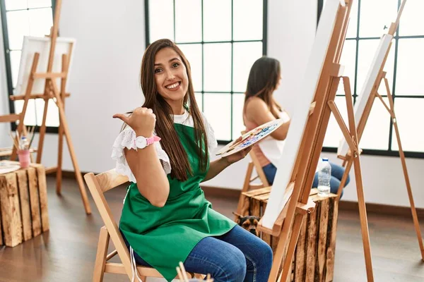 若いヒスパニック系のアーティストの女性は 手の笑顔でOkジェスチャーを行うアートスタジオでキャンバス上で絵を描く 幸せな顔で指を通して見て目 — ストック写真