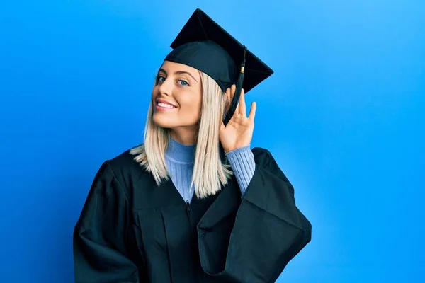 卒業キャップと儀式用のローブを身に着けている美しいブロンドの女性は噂やゴシップに耳を傾ける耳の上に手で笑顔 聴覚障害の概念 — ストック写真