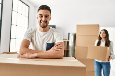 Genç İspanyol adam mutlu bir şekilde gülümsüyor. Yeni evindeki karton üzerine yaslanıyor..