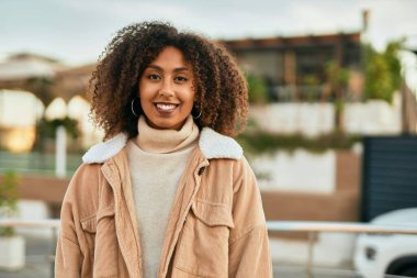 Genç Afrikalı Amerikalı kadın gülümseyerek şehirde mutlu mesut duruyor..