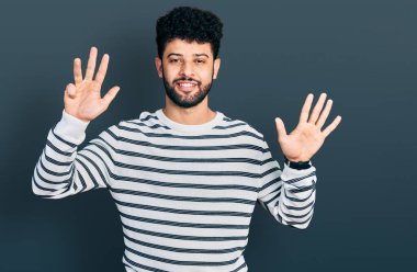 Sakallı, sıradan çizgili süveter giyen genç Arap adam dokuz numaralı parmaklarıyla kendini beğenmiş ve mutlu gülümserken onu gösteriyor.. 