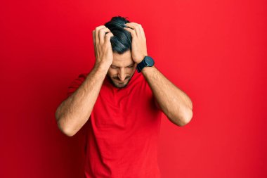 Genç İspanyol adam gündelik kırmızı t-shirt giyiyor. Baş ağrısı çekiyor, çaresiz ve stresli. Çünkü ağrı ve migren. Eller başının üstünde.. 