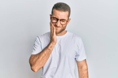 Günlük kıyafetler giyen ve gözlük takan genç beyaz bir adam diş ağrısı ya da diş hastalığından dolayı ağızlarına acı dolu bir ifadeyle dokunuyor. dişçi 