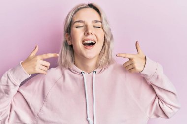 Genç sarışın kız parmaklarıyla dudaklarını gösterip kahkahalarla gülüyor.. 