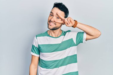 Gündelik kıyafetler giyen genç İspanyol adam barış sembolü yapıyor. Yüzünde parmaklar, gülümseyerek zaferi gösteriyor. 