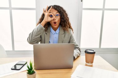 Güzel bir İspanyol iş kadını ofisinde oturmuş laptopla çalışıyor. Şok olmuş bir jest yapıyor. Şaşırmış bir yüz ve parmaklarından bakan bir gözle. İnançsız ifade. 