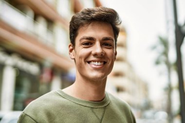 Genç İspanyol adam gülümseyerek şehirde mutlu mesut dikiliyor..