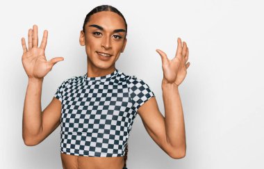 Makyaj yapan, uzun saçlı, modern kıyafetler giyen İspanyol transseksüel adam 10 numaralı parmaklarıyla işaret ederken kendinden emin ve mutlu gülümsüyor.. 