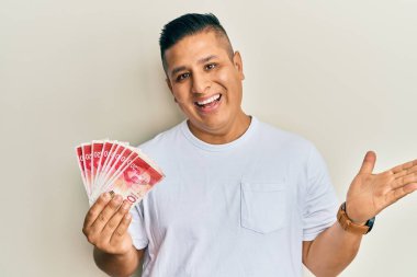 Elinde 20 İsrail parası olan genç Latin adam başarıyı mutlu bir gülümsemeyle ve kazanan ifadeyle kutluyor. 
