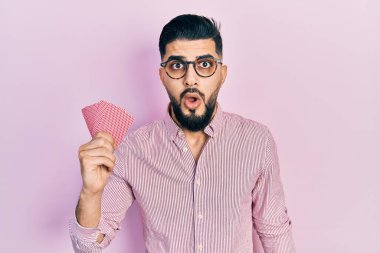 Poker kartları tutan yakışıklı bir adam ağzı açık kalmış, korkmuş ve hayrete düşmüş. 