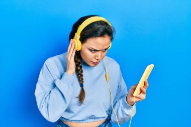 Akıllı telefon ve kulaklık kullanan genç İspanyol kız şüpheci ve gergin, sorun yüzünden surat asıyor. negatif kişi. 