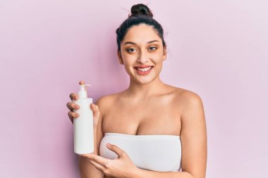 Güzel orta doğulu kadın elinde kozmetik nemlendirici yüz kremi tutuyordu. Pozitif ve mutlu görünüyordu. Kendine güvenen bir gülümsemeyle dişlerini gösteriyordu. 