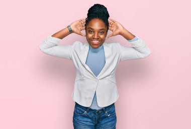 Genç Afro-Amerikalı kadın iş kıyafetleri içinde rahatlıyor ve esniyor, kolları ve elleri başının arkasında ve boynunun arkasında mutlu bir şekilde gülümsüyor. 