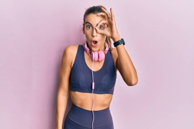 Spor kıyafetleri giyen, kulaklık takan, şaşırmış yüzüyle şaşırmış, parmaklarından bakan güzel bir kadın. İnançsız ifade. 