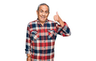 Üst düzey İspanyol adam günlük kıyafetler giyiyor mutlu ve pozitif gülümsüyor, başparmağıyla mükemmel ve onay işareti yapıyor. 