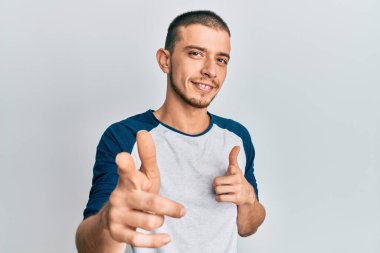 Gündelik kıyafetler giyen İspanyol genç adam mutlu ve komik yüzüyle kamerayı işaret ediyor. iyi enerji ve titreşimler. 