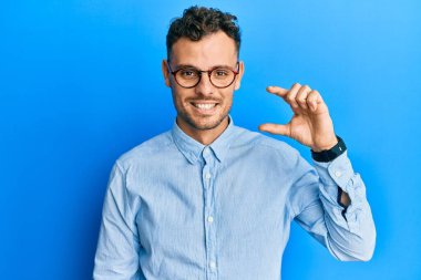 Günlük kıyafetler giyen, gözlüklü, gülümseyen, kendine güvenen, el hareketi yapan, parmaklarıyla işaret yapan ve kameraya bakan genç İspanyol bir adam. ölçüm kavramı. 