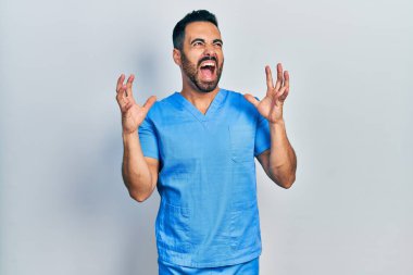 Sakallı, mavi erkek hemşire üniforması giyen yakışıklı, deli gibi bağıran, sinirli ifadeli ve kollarını kaldırmış bir İspanyol. hüsran kavramı. 