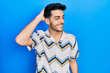 Gündelik kıyafetler giyen genç İspanyol adam gülümseyerek saçlarına dokunarak el hareketleriyle çekici ve modaya uygun bir poz veriyor. 