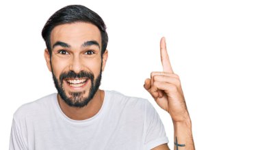 Gündelik beyaz tişört giyen genç İspanyol adam başarılı bir fikri işaret ediyor. Heyecanlı ve mutlu. Bir numara.. 