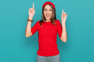 Genç esmer kadın gündelik kıyafetler giyip şaşkın şaşkın gülüyor, parmaklarıyla işaret ediyor ve kollarını kaldırıyordu.. 