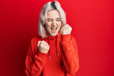 Sıradan kıyafetler giyen genç sarışın kız pozitif ve mutlu görünüyor. Kendine güvenen bir gülümsemeyle ayakta duruyor ve dişlerini gösteriyor. 