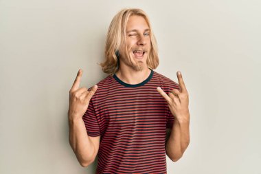 Kafkasyalı, uzun saçlı, taş jestler yapan, kameraya seksi bir ifadeyle bakan, neşeli ve mutlu yüzlü bir genç.. 