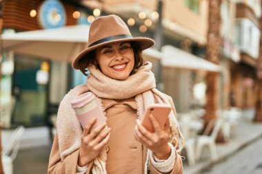 Genç İspanyol kadın akıllı telefon kullanıyor ve şehirde kahve içiyor..