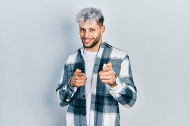 Modern boyalı saçlı, sıradan gömlekli, neşeli ve komik yüzlü genç İspanyol bir adam kamerayı işaret ediyor. iyi enerji ve titreşimler. 