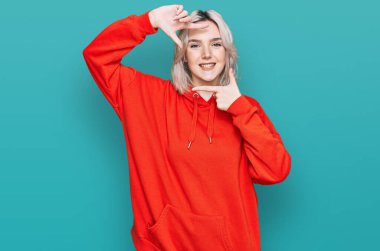 Gündelik kıyafetler giyen, gülümseyen, elleri ve parmakları gülen yüzlü, çerçeveli genç sarışın kız. yaratıcılık ve fotoğrafçılık kavramı. 