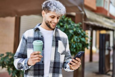 Genç İspanyol adam şehirde akıllı telefon kullanarak mutlu gülümsüyor..