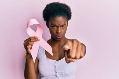 Elinde pembe kanser kurdelesi olan genç Afro-Amerikalı kız kamerayı işaret ediyor ve sen kendine güvenen, ciddi görünüyorsun. 