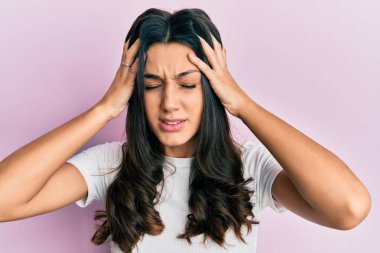 Genç İspanyol kadın gündelik beyaz tişört giyiyor. Baş ağrısı çekiyor, çaresiz ve stresli. Çünkü ağrı ve migren. Eller başının üstünde.. 